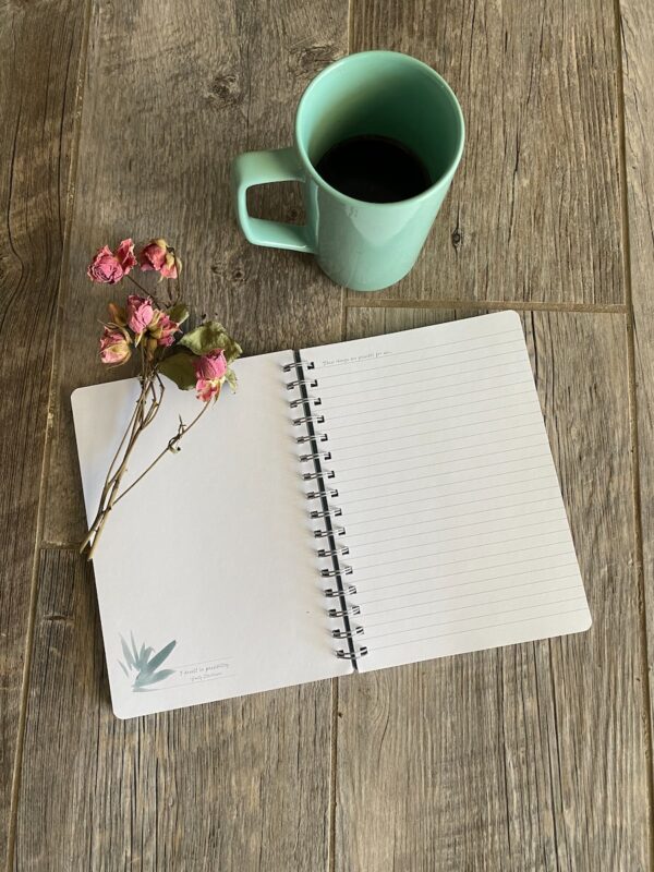 white notebook beside white ceramic mug on brown wooden table